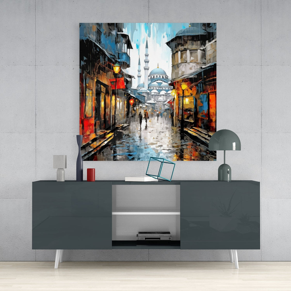 Rainy street and mosque glass wall art above a dark gray sideboard with a small lamp