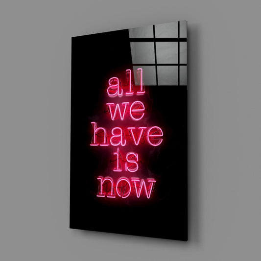 All we have is now pink neon glass wall art on a gray wall with a soft window reflection