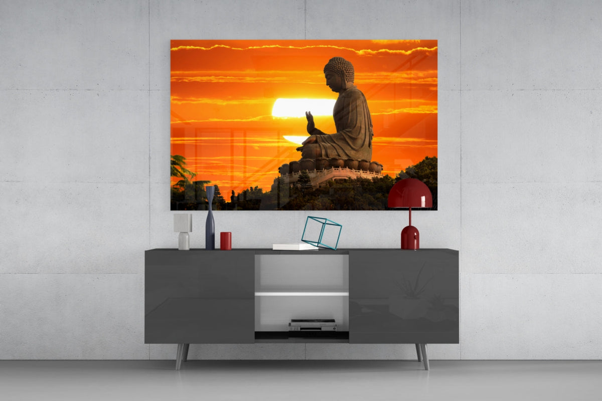 Buddha at sunset glass wall art on a concrete wall above a dark gray sideboard with a red lamp