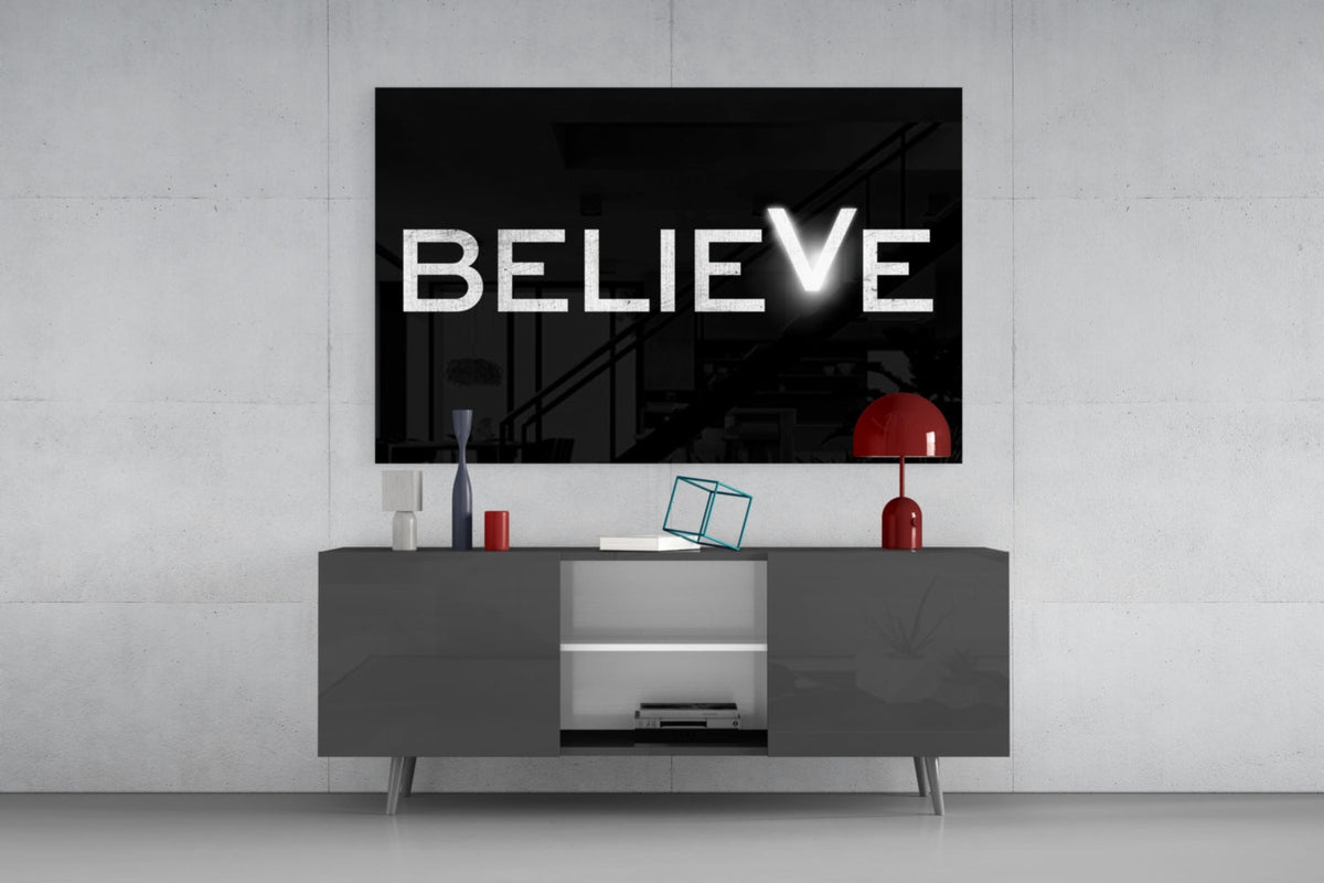 Believe on black with a glowing V glass wall art above a dark gray sideboard with a table lamp