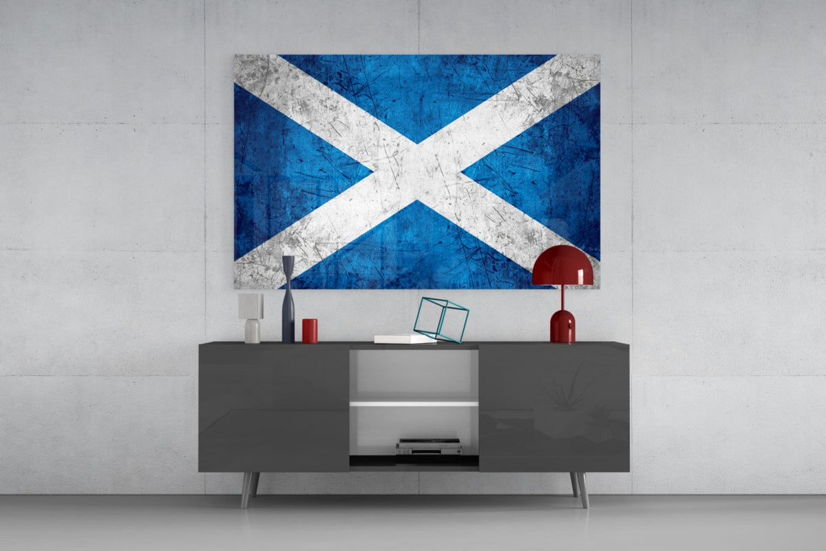 Scratched Scotland flag glass wall art above a gray sideboard with a red lamp on a pale concrete wall
