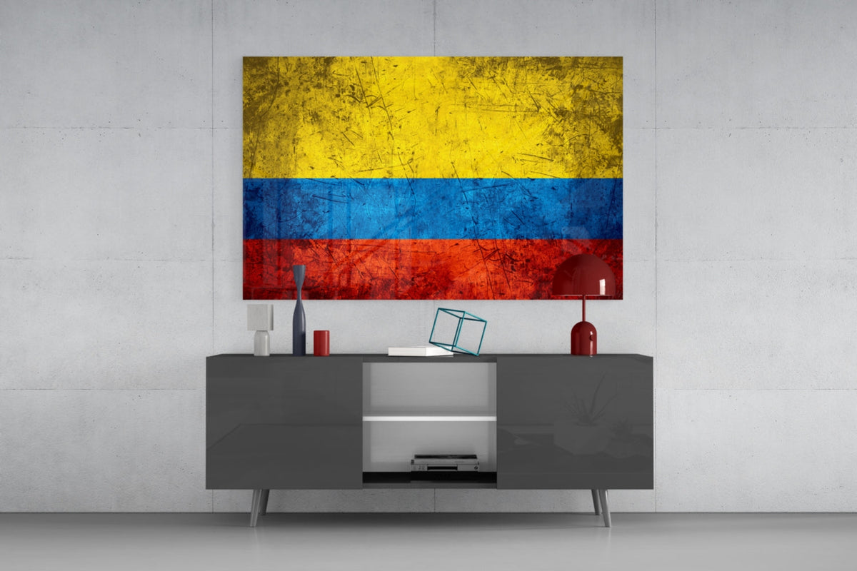 Weathered Colombia flag glass wall art above a dark gray media console with a red table lamp