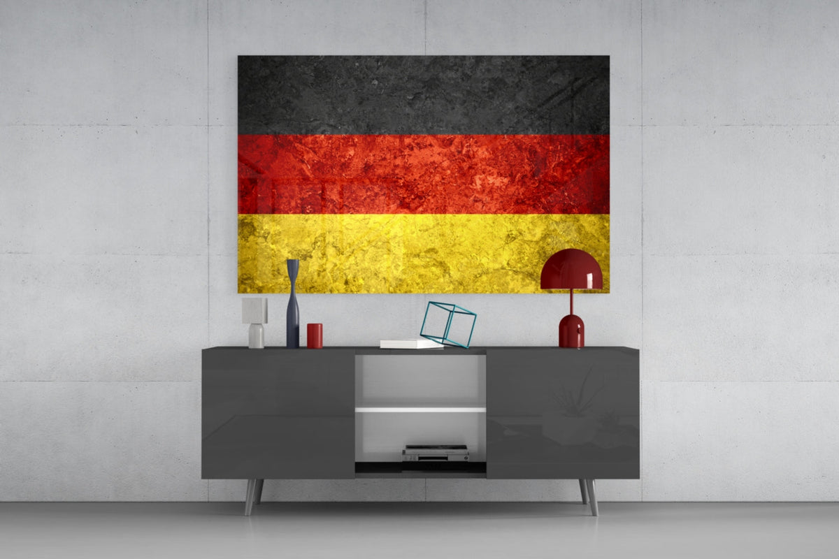 Weathered Germany flag glass wall art above a dark gray media console with a red table lamp