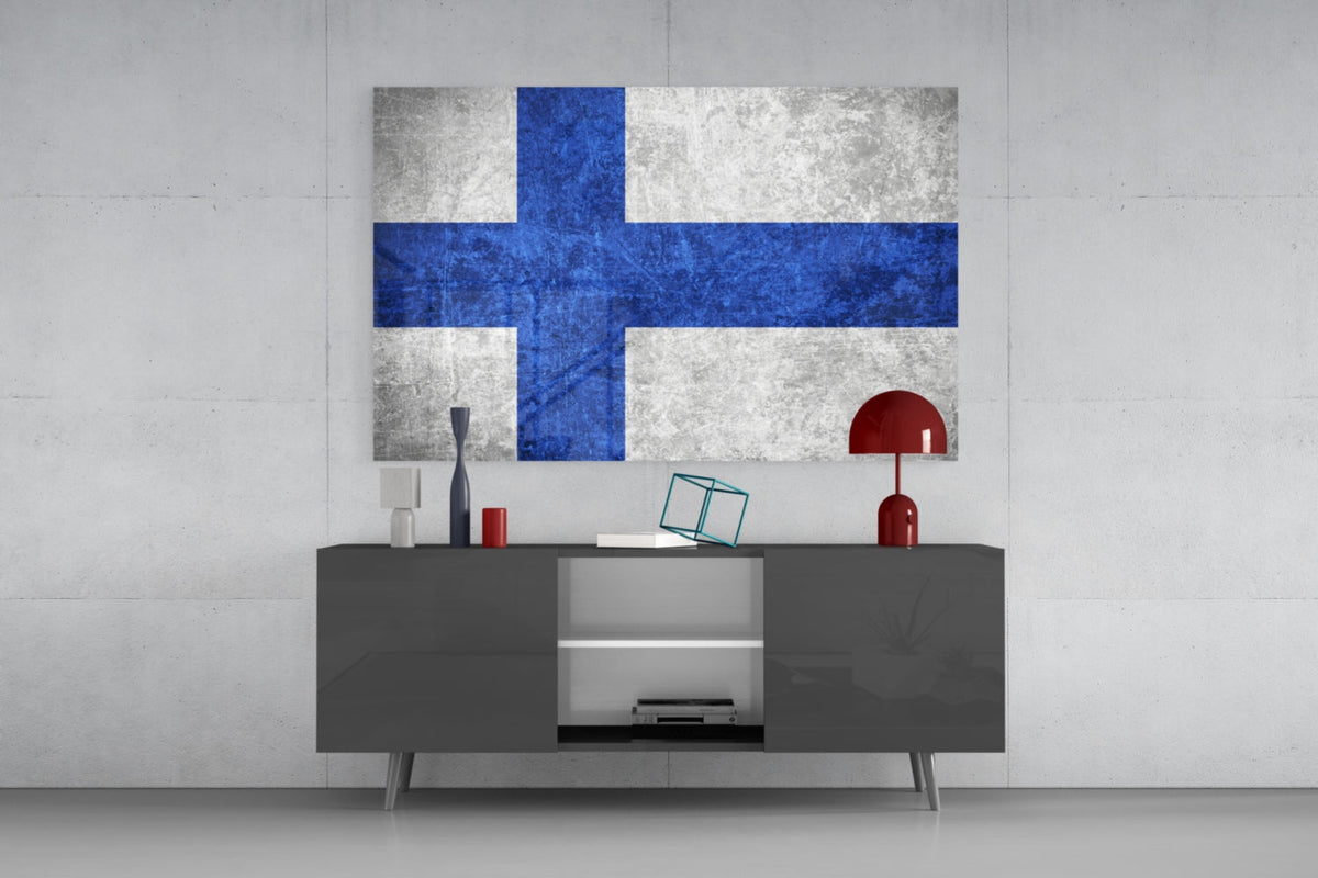 Weathered Finland flag glass wall art above a dark gray media console with a red table lamp