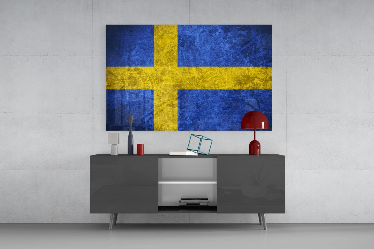 Weathered royal blue Sweden flag glass wall art above a dark gray media console with a red table lamp