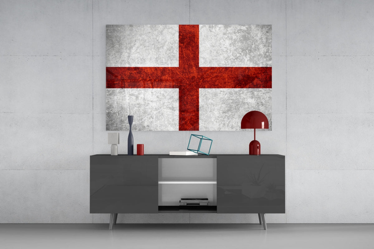 Crimson cross England flag glass wall art above a gray sideboard with a red lamp on a pale concrete wall