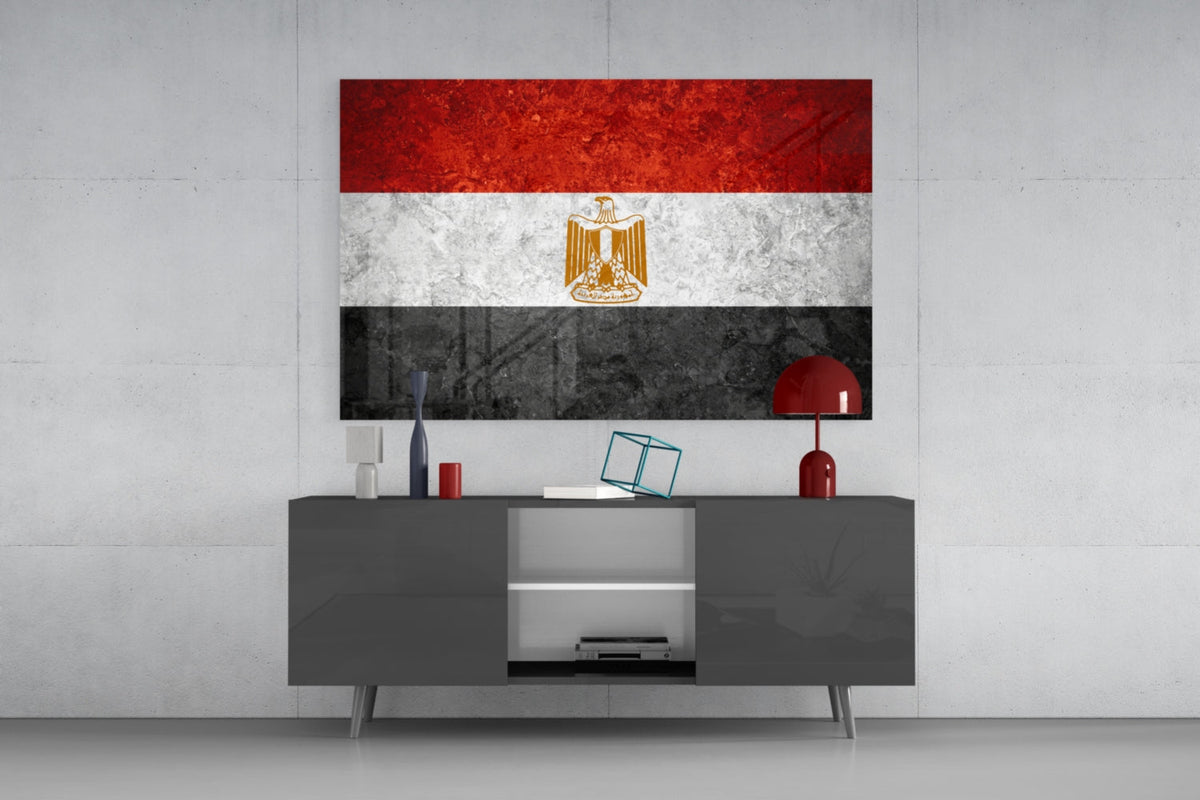 Weathered Egypt flag glass wall art above a dark gray media console with a red table lamp