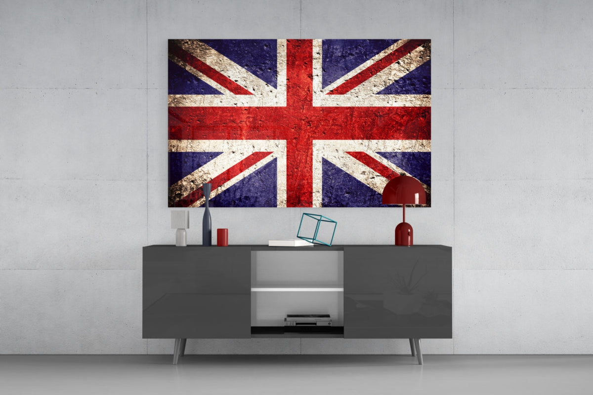 Worn stone United Kingdom flag glass wall art above a gray sideboard with a red lamp on a pale concrete wall