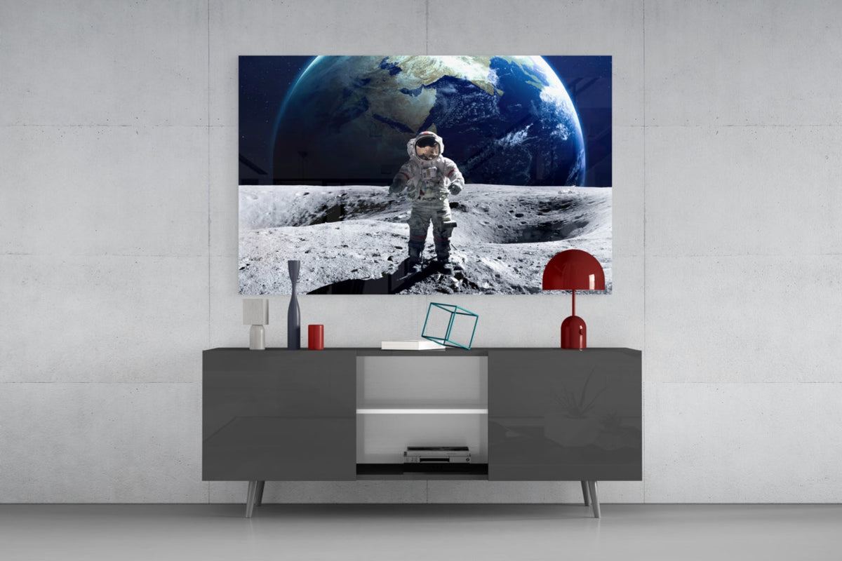 Astronaut on the moon glass wall art above a dark gray sideboard with a red lamp on a concrete wall
