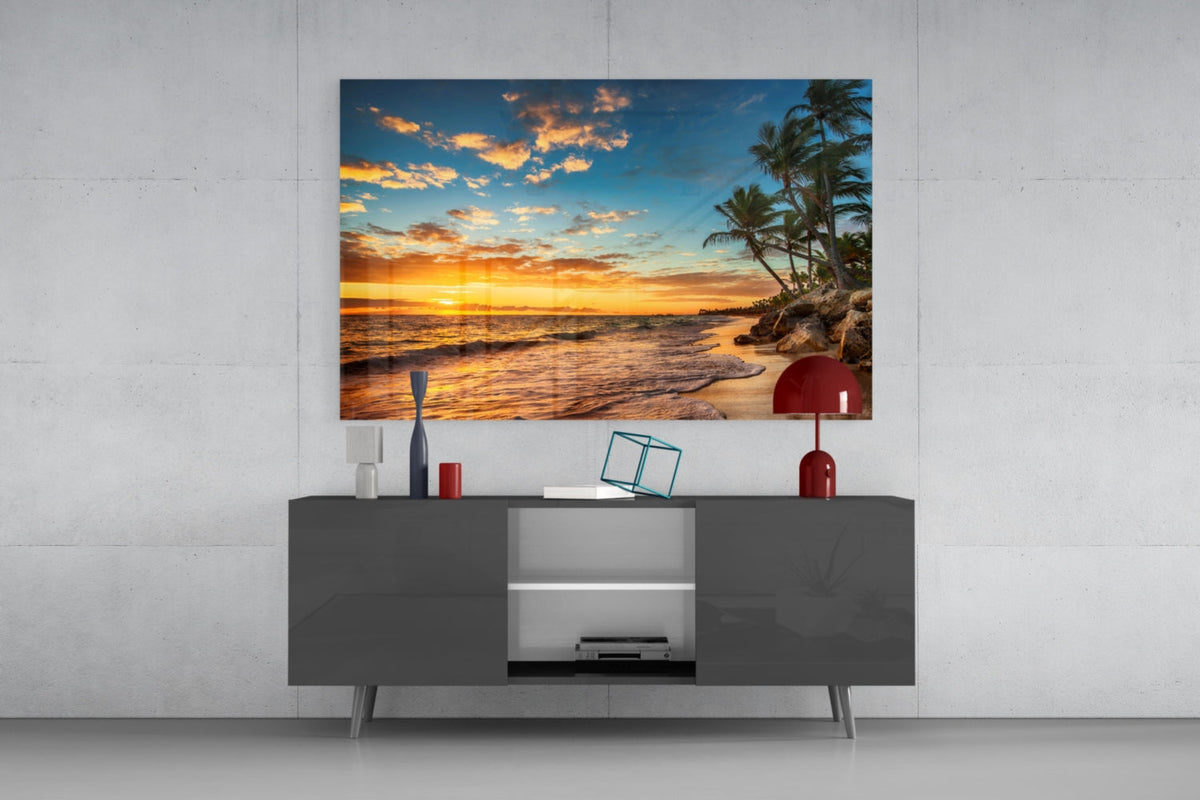 Tropical beach sunset glass wall art above a dark gray sideboard with a red lamp on a concrete wall
