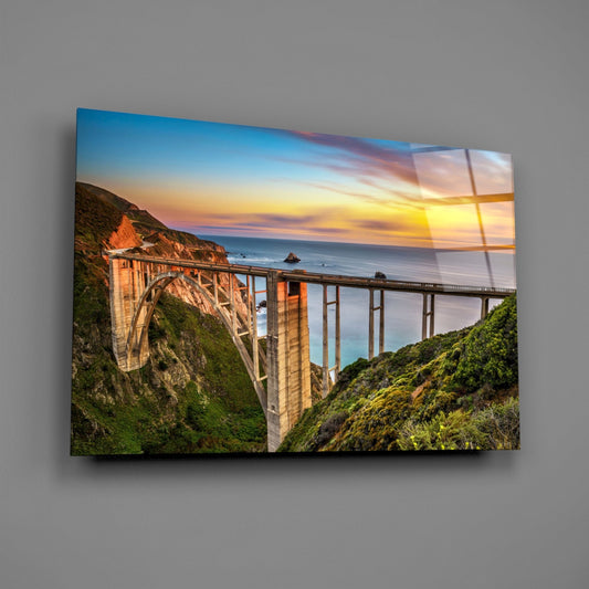 Bixby Creek Bridge glass wall art angled on a gray backdrop with light reflecting off the glossy front