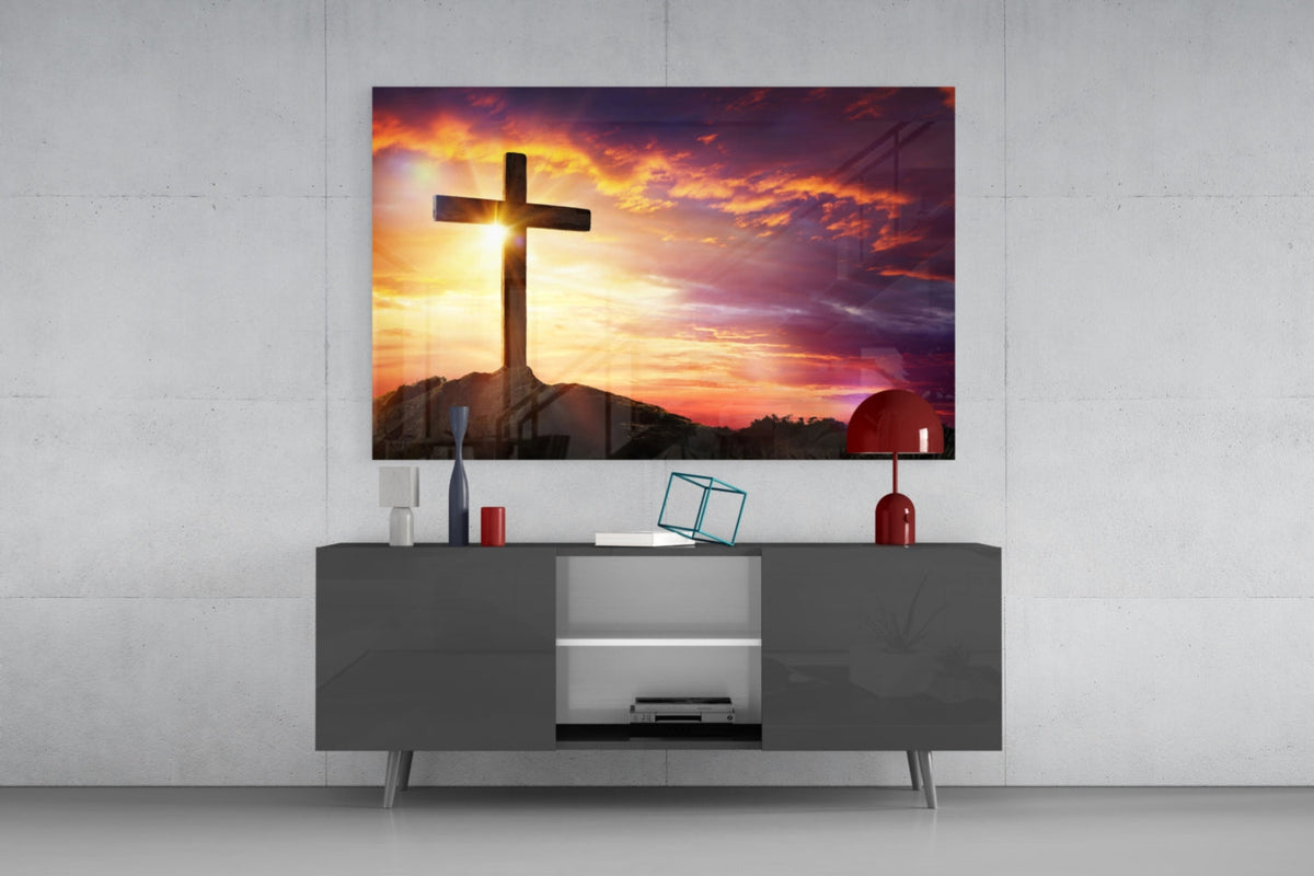 Wooden cross at sunset glass wall art above a dark gray sideboard with a small red lamp
