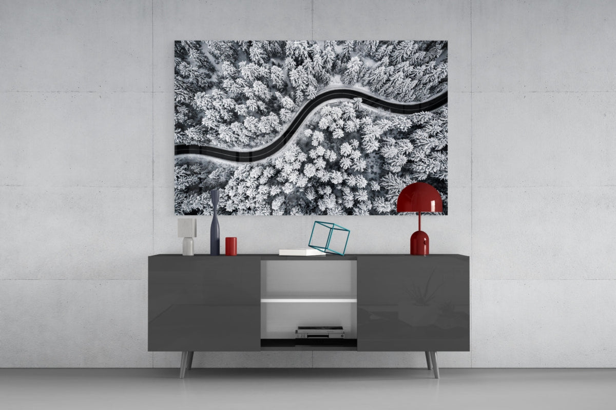 Snowy forest winding road glass wall art above a dark gray sideboard with a red table lamp