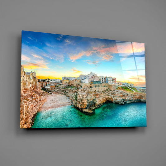 Clifftop coastal village glass wall art angled on a gray backdrop with light reflecting off the glossy front