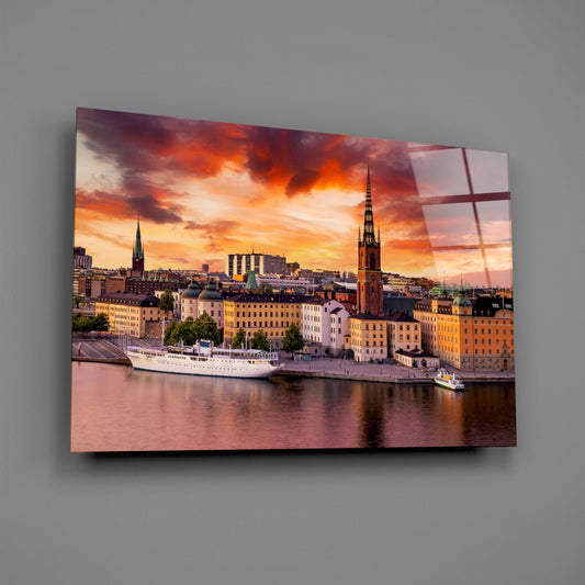 Stockholm waterfront at sunset glass wall art on a plain gray wall, angled to show the glossy surface