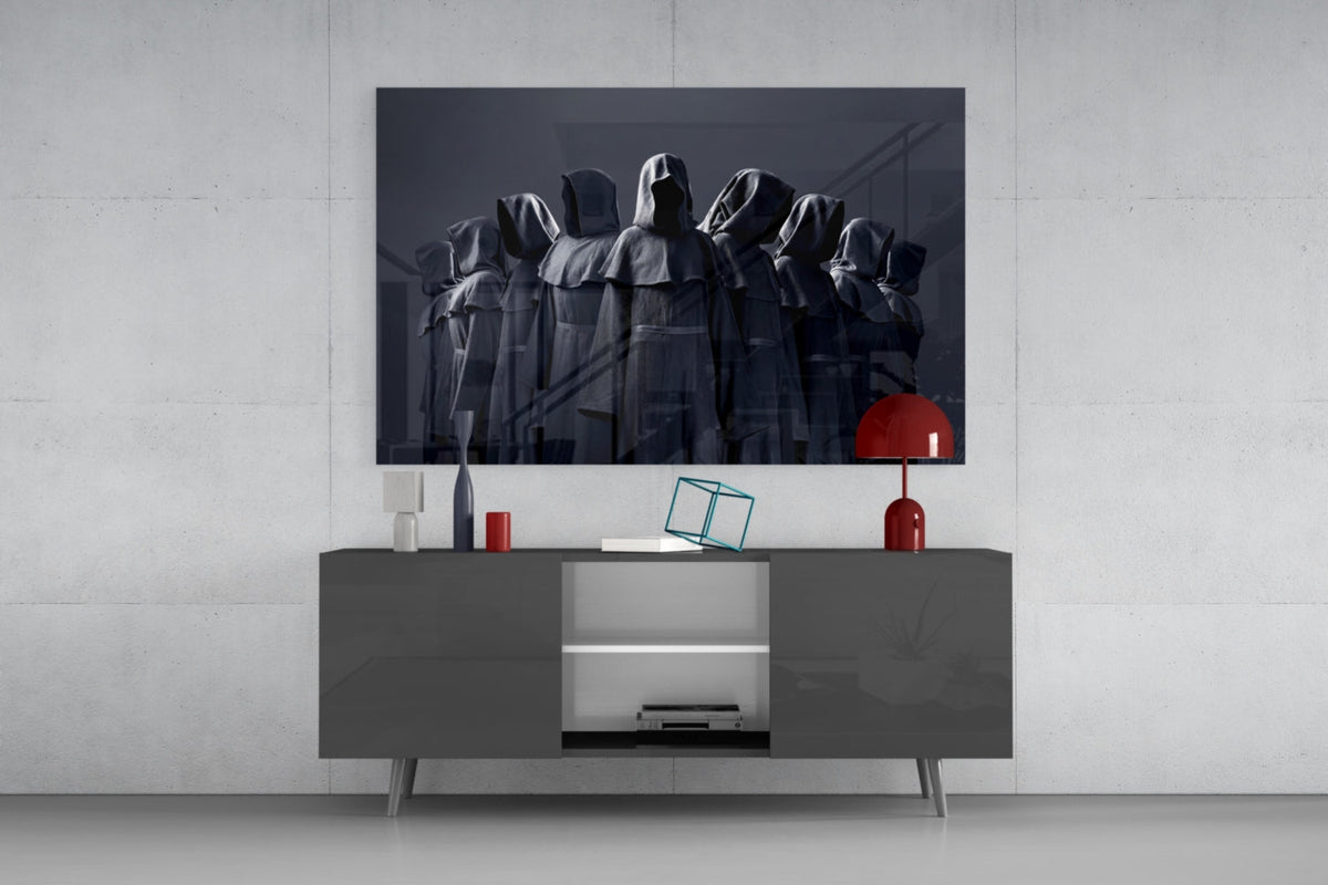 Hooded cloaked figures glass wall art above a gray sideboard with a red lamp