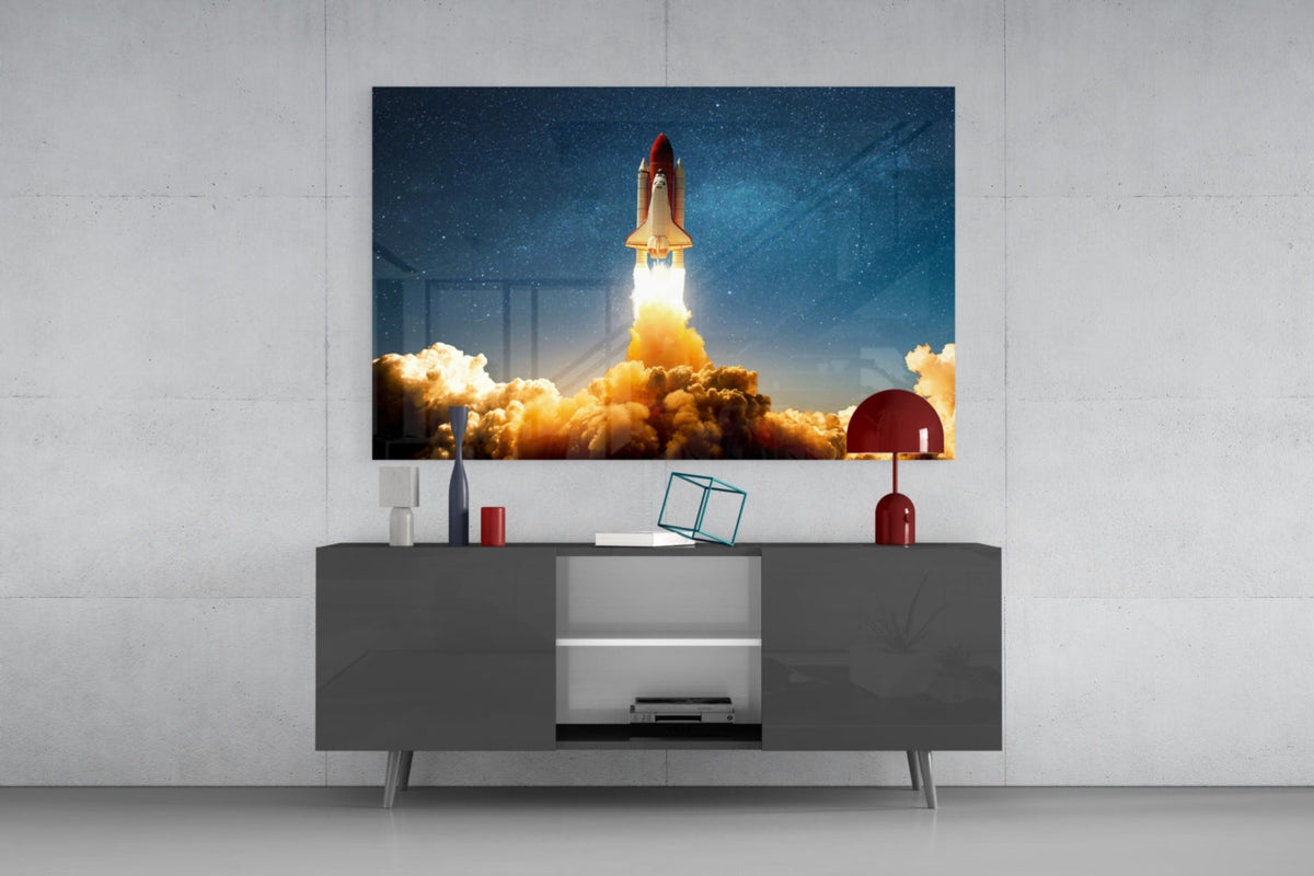 Shuttle launch glass wall art above a dark gray sideboard with a red lamp on a concrete wall