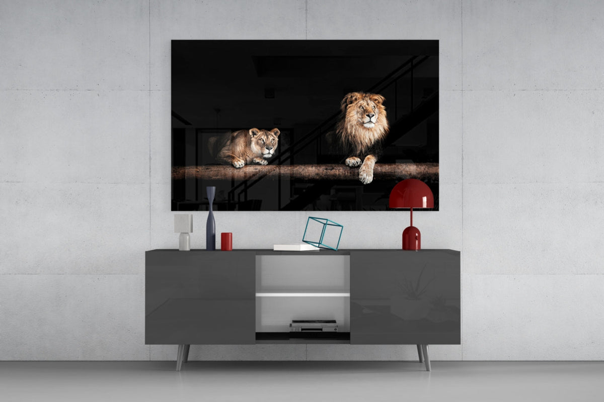 Lion and lioness on a log glass wall art above a dark gray sideboard with a small red lamp