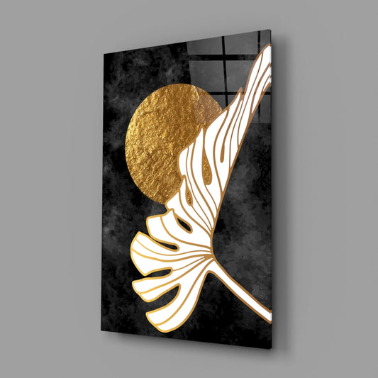 Gold moon and monstera glass wall art on a gray wall with a window reflected in the glossy front