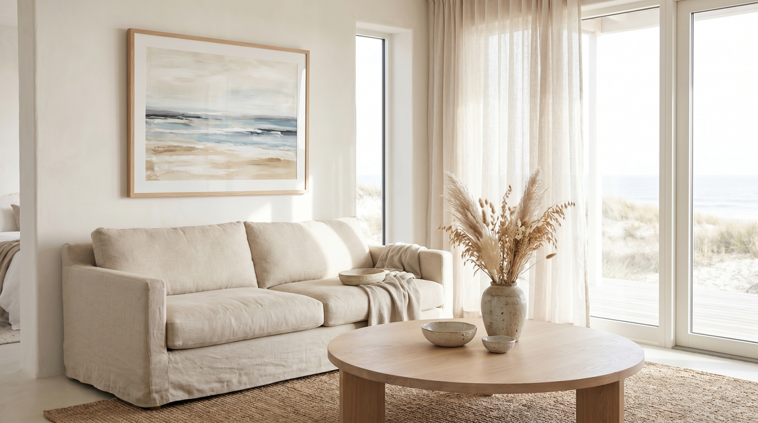 Airy modern coastal living room in muted blue, sand, and warm white with a large framed abstract horizon print over a linen sofa