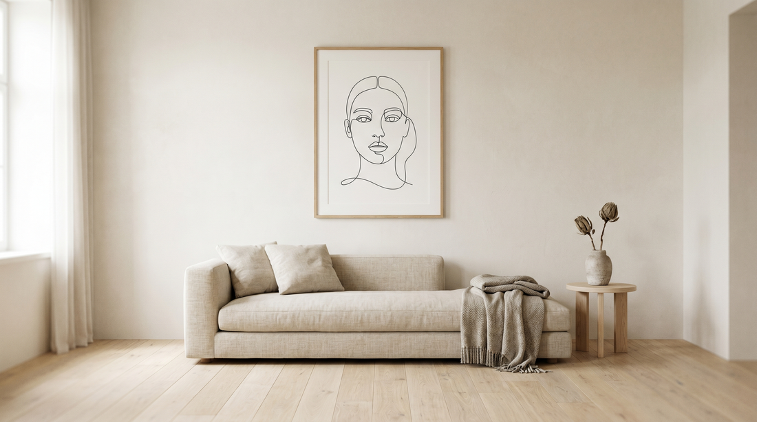 Calm minimalist living room with one framed line-art print above a low sofa and plenty of empty wall