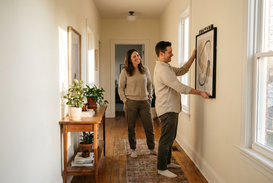 Personalized wall decor: a couple hanging a framed print together in a hallway