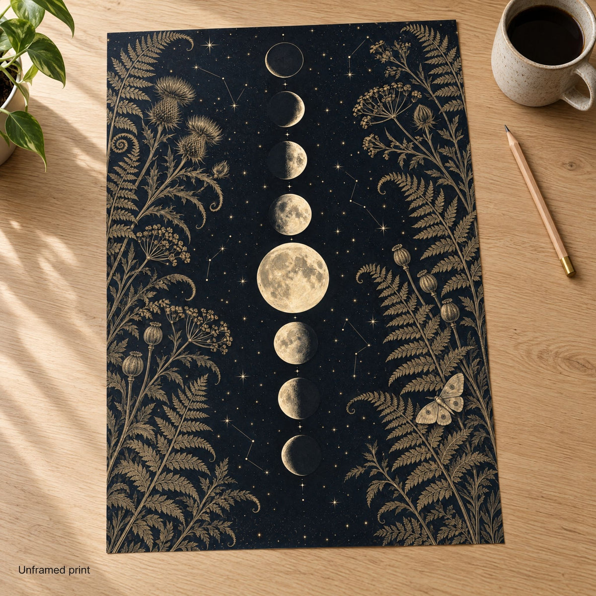 Unframed moon phase art print on matte paper, lying flat on a light oak desk beside a mug