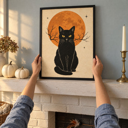 Black cat and full moon print in a black frame being set on an October mantel beside white pumpkins