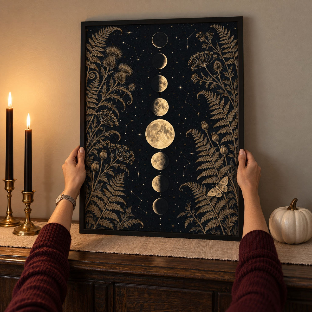 Framed black and gold moon print being set on an October dining sideboard between black taper candles