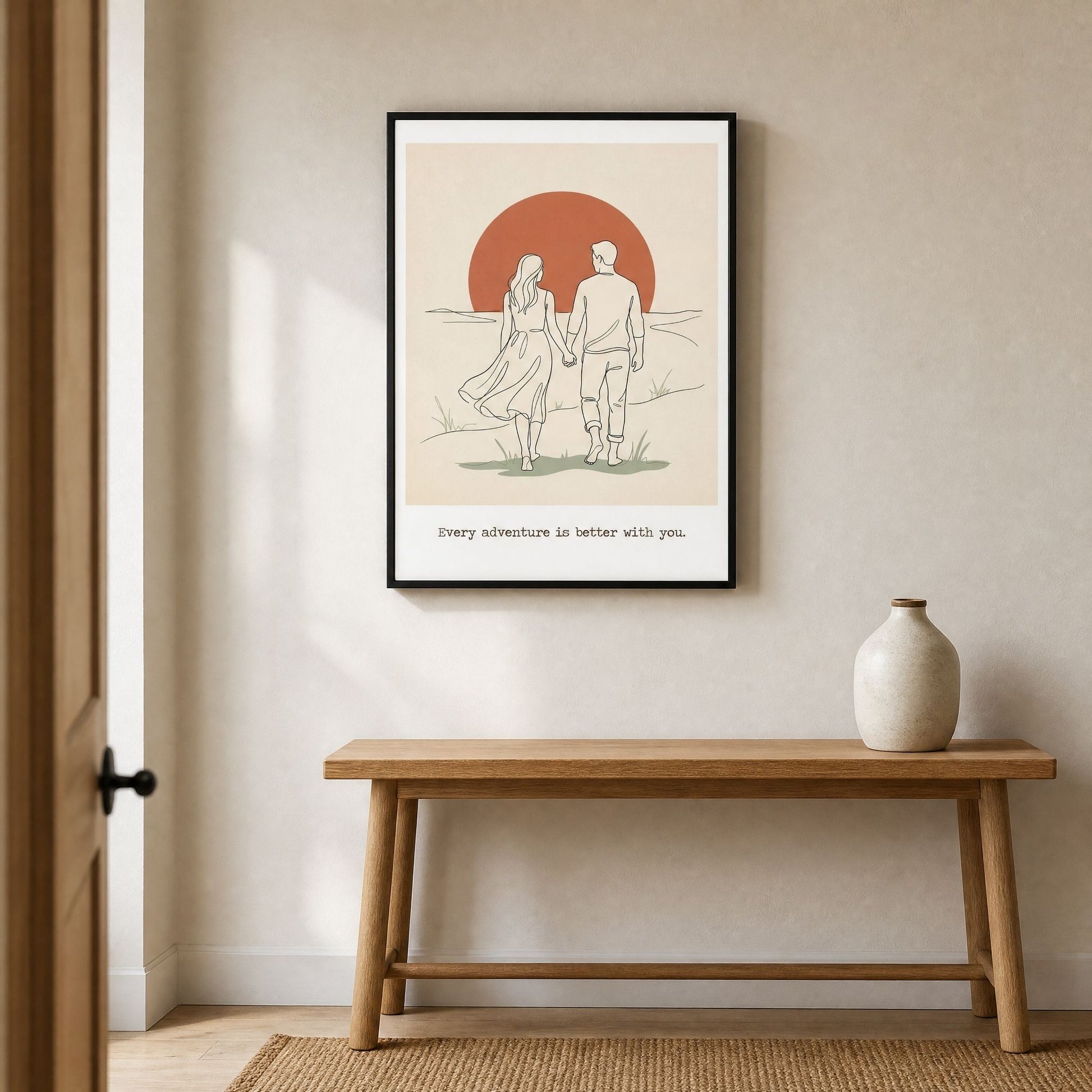 Framed wall art above an oak bench in a bright entryway, with a pale ceramic vase beside it.