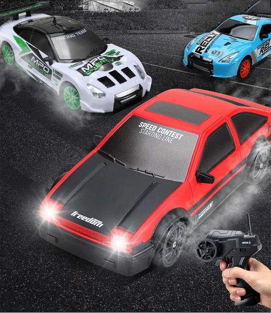 Three remote control cars on a racetrack with a hand holding a remote control.