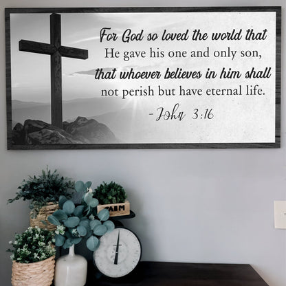 Black and white cross on a hilltop with John 3:16 in black script and type on white