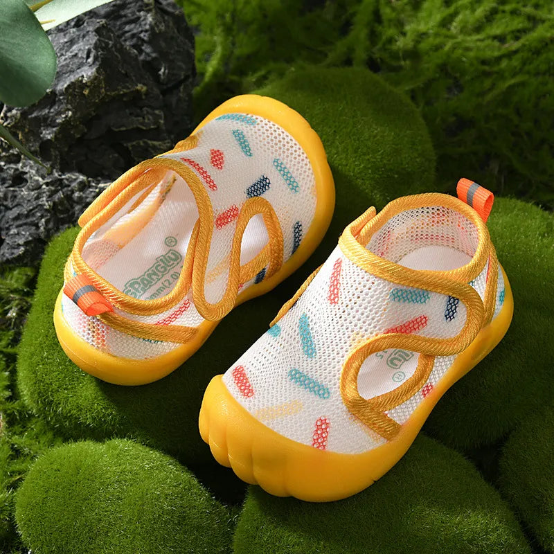 Pair of yellow children's water sandals with colorful patterns on a green moss background