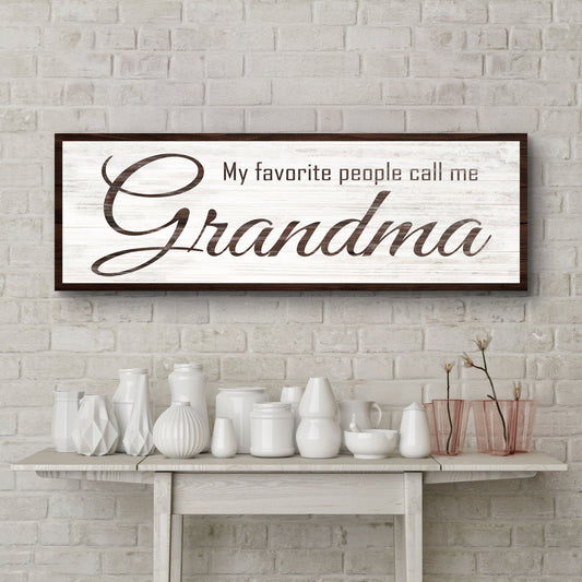 My Favorite People Call Me Grandma canvas sign in brown script on white, above a shelf of white vases on a brick wall