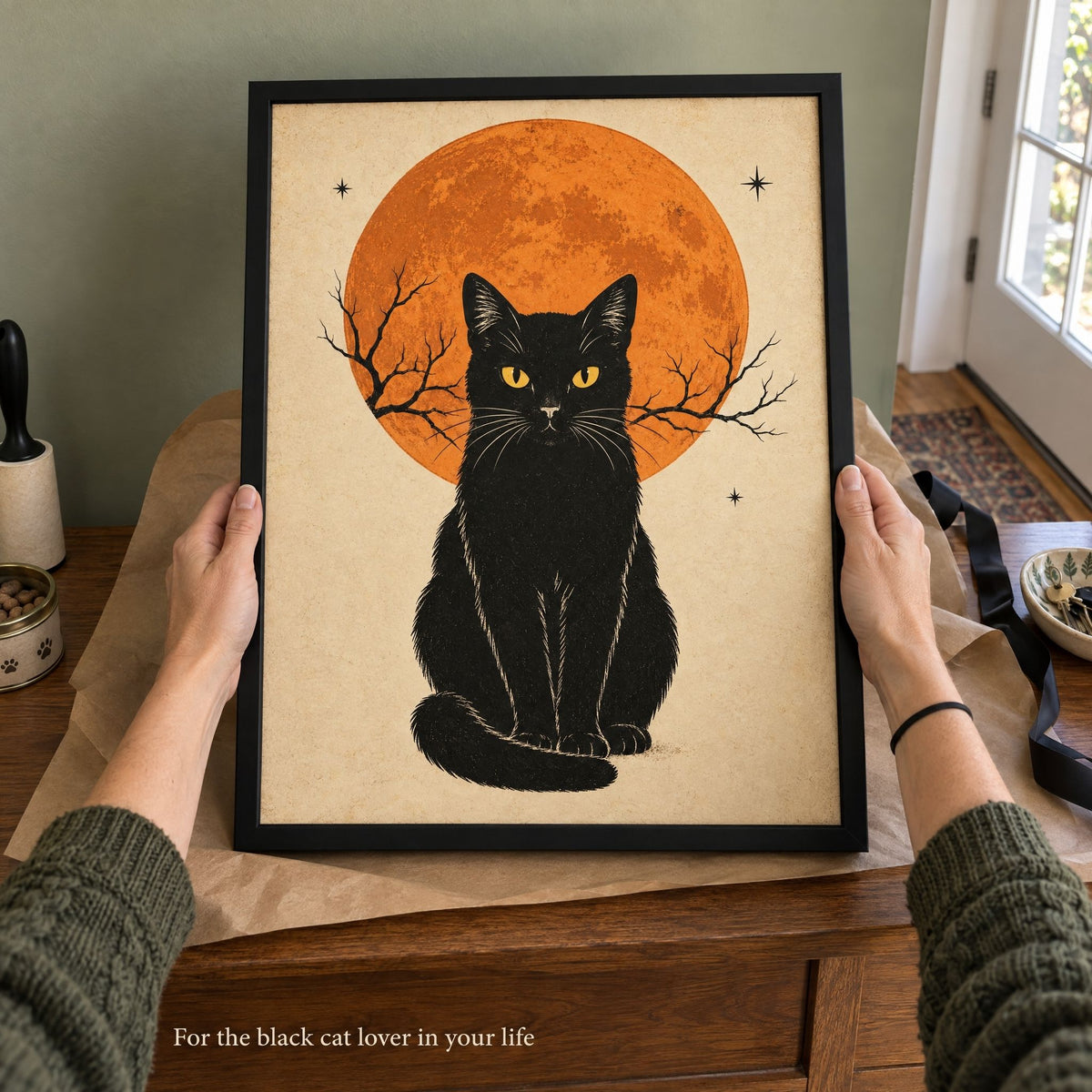 Hands lifting the framed black cat print from its kraft paper wrapping on a hall console, a gift for a cat lover
