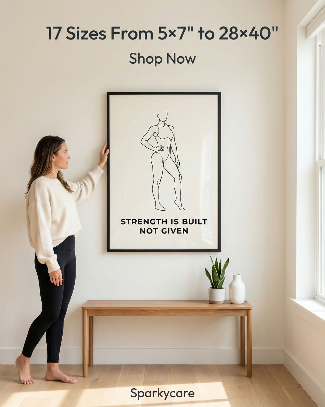 Woman hanging a framed artwork with motivational quote in a minimalistic room.