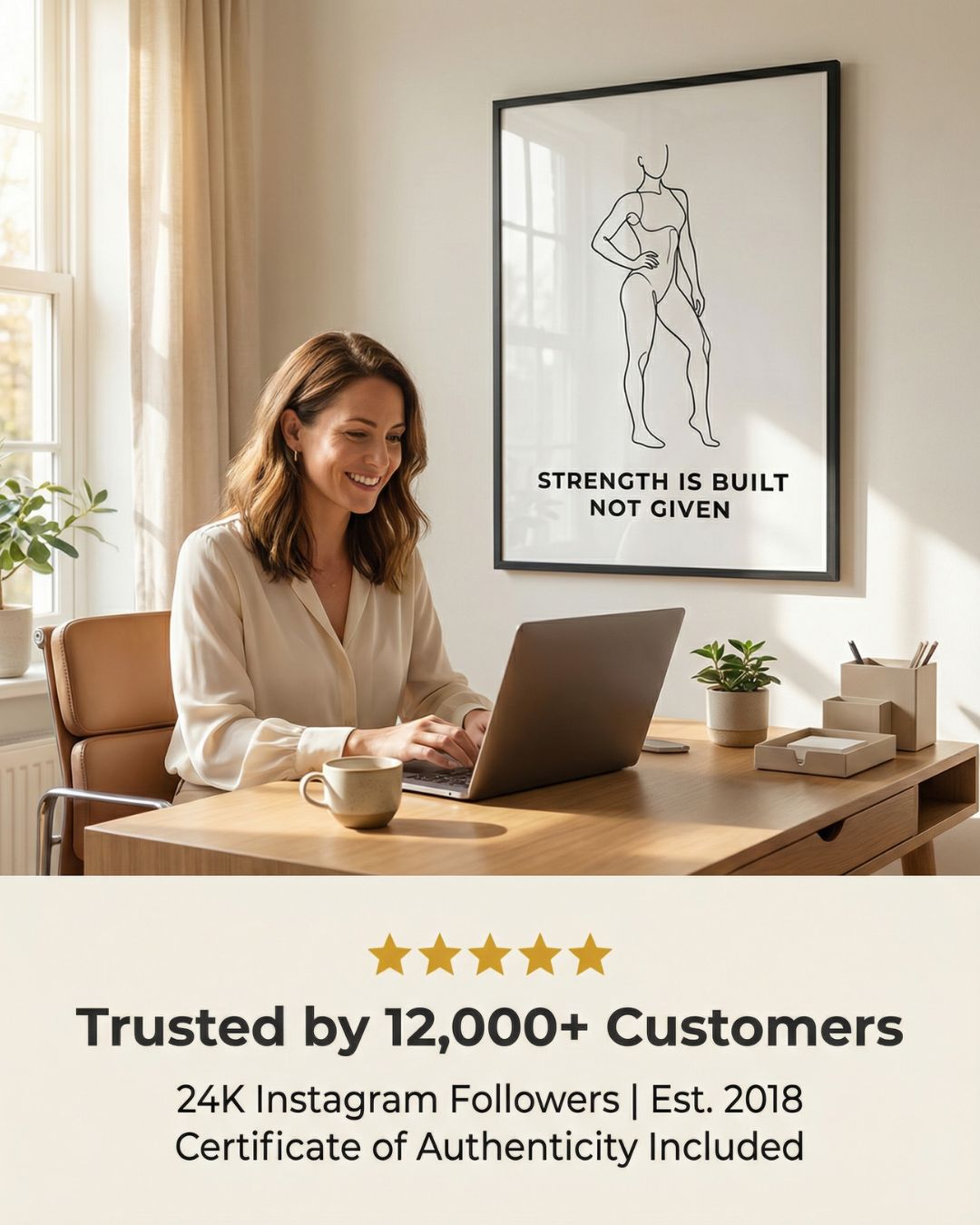 Woman working at a desk with a motivational poster on the wall, featuring text 'Strength is built, not given'.