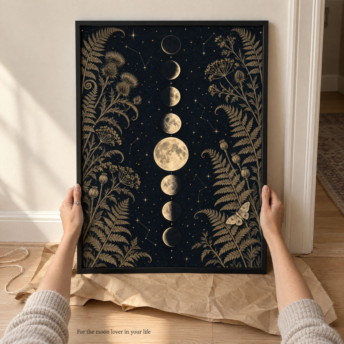 Hands steadying a large framed moon phase print just unwrapped from kraft paper, a gift for a moon lover