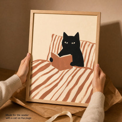 Hands holding the framed black cat reading print over a linen bed, showing its scale in the room