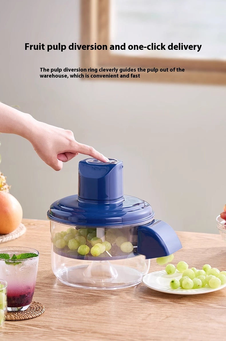 Blue fruit pulper on a wooden table with grapes and a hand pressing a button.