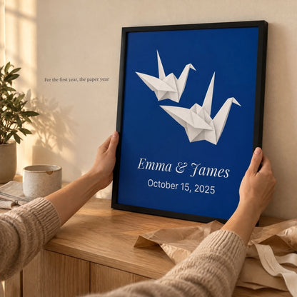 Hands holding the framed paper cranes anniversary print above a wooden table