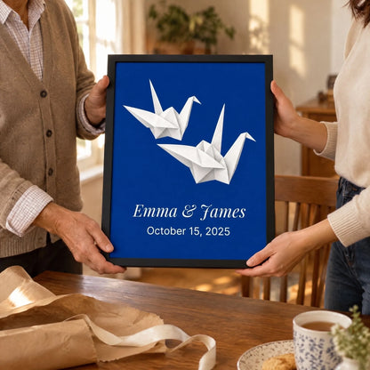 A framed paper cranes anniversary print passed between two people at a table, wrapping beside it