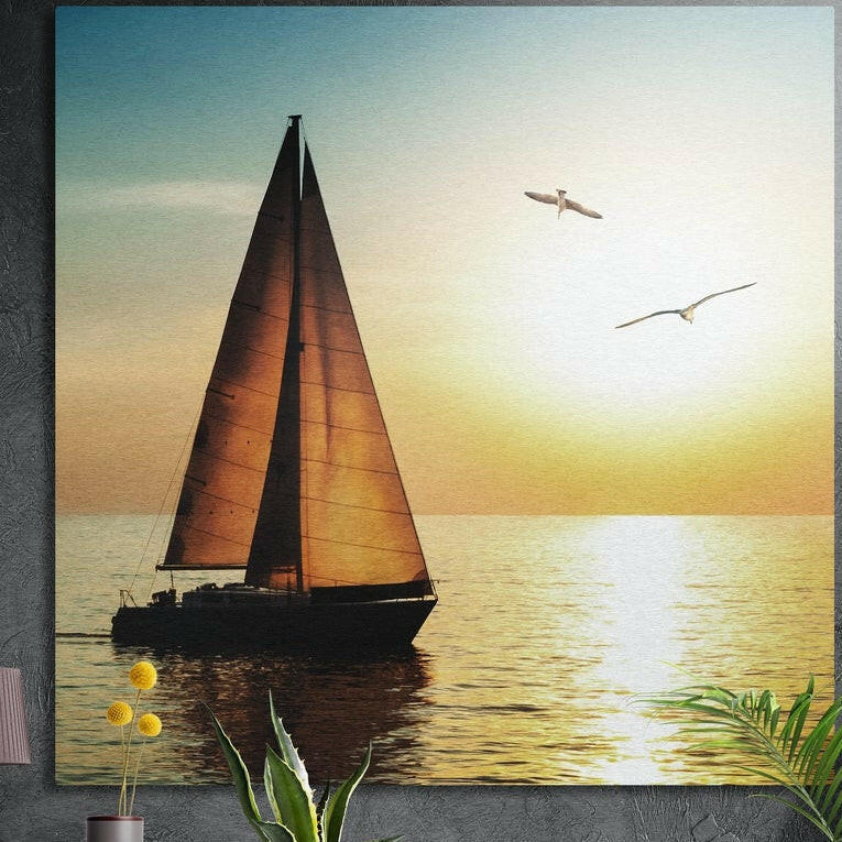 Sailboat with amber sails on a calm sea at golden sunset, brushed aluminum wall art on a dark wall behind plants