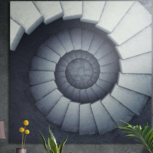 White stone spiral staircase seen from above in cool gray, brushed aluminum wall art on a dark wall behind plants