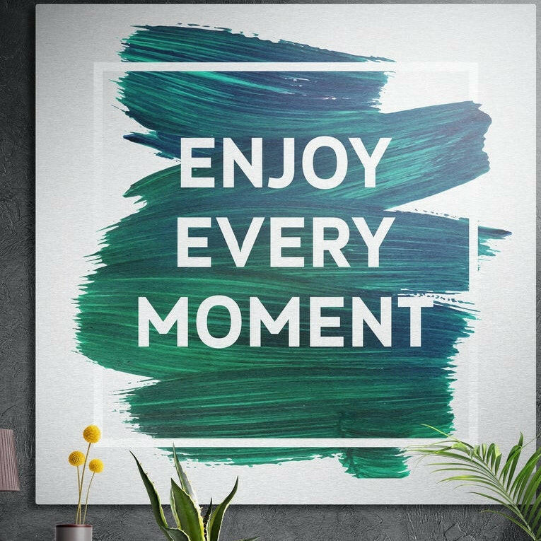 Bold white motivational lettering on green brushstrokes, brushed aluminum wall art on a concrete wall behind plants