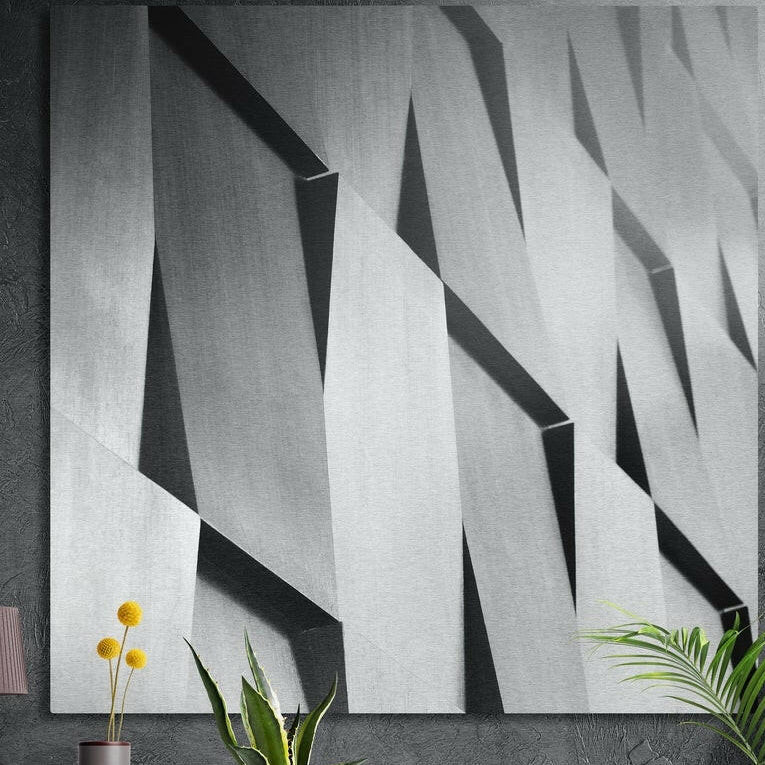 Angled gray concrete facade panels in light and shadow, brushed aluminum wall art on a concrete wall behind plants