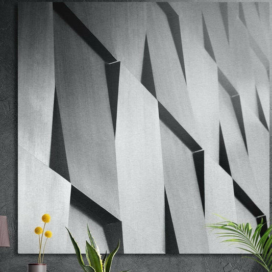 Angled gray concrete facade panels in light and shadow, brushed aluminum wall art on a concrete wall behind plants