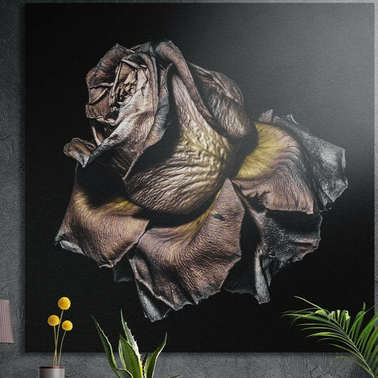 Silver and gold metallic rose in full bloom on black, brushed aluminum wall art on a dark wall behind plants