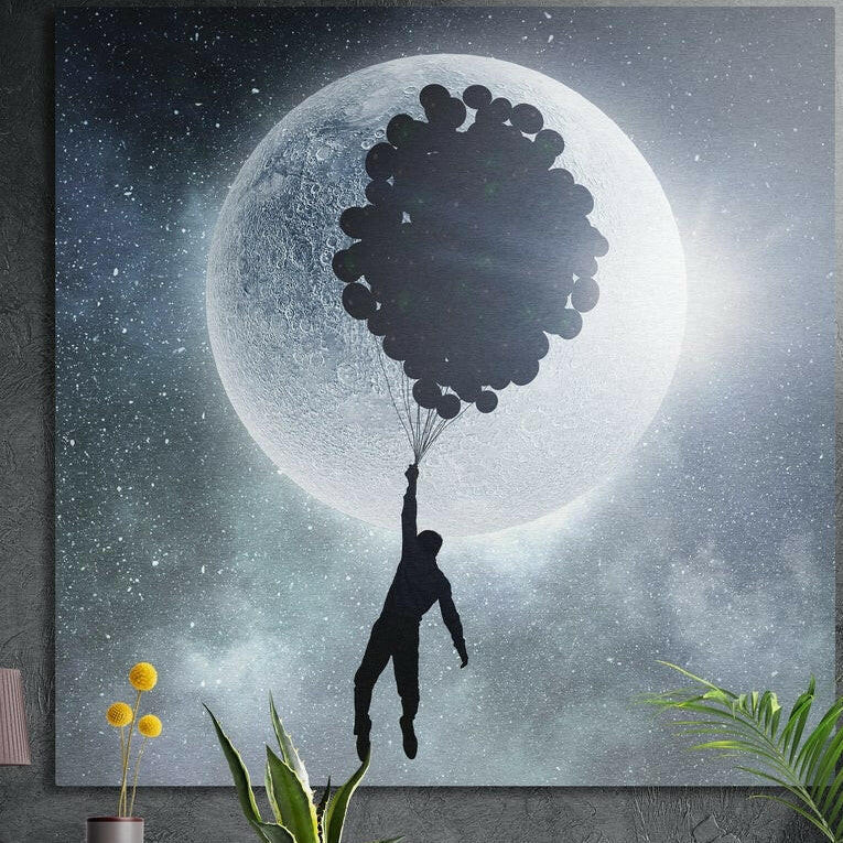 Silhouette of a man holding balloons over a glowing full moon, brushed aluminum wall art on a dark wall with plants