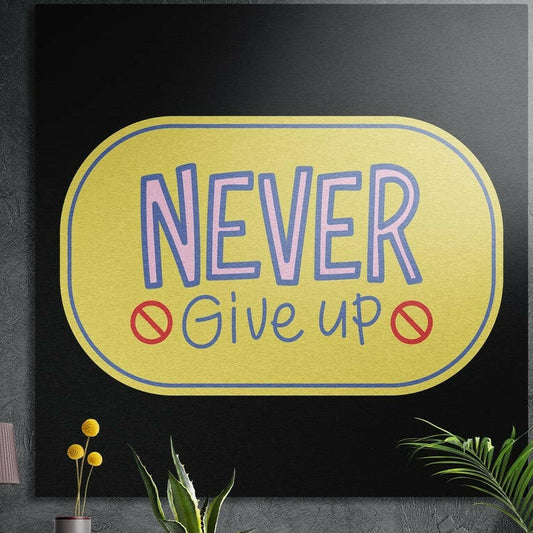 Never give up lettering in a rounded yellow badge on black, brushed aluminum wall art on a dark wall behind plants